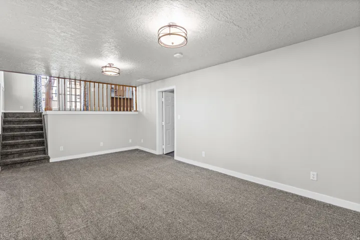 Spacious carpeted area featuring an open staircase with a wooden railing, neutral wall color, and flush mount lighting fixtures