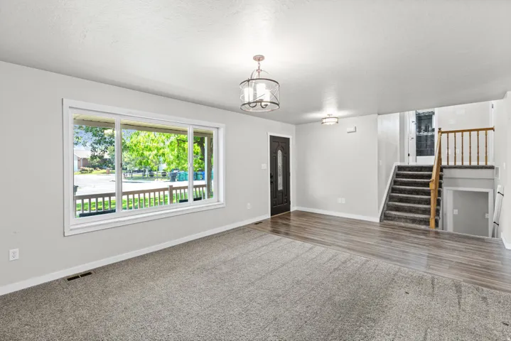 Expansive living area with wood-finish flooring, broad window, and a multi-level staircase with wood railing