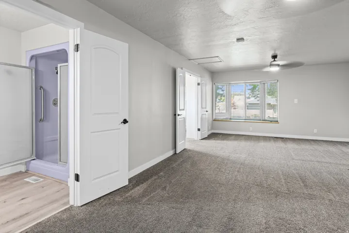 Spacious primary suite featuring multiple large windows flooding the space with natural light, polished concrete ceiling with integrated recessed lighting, neutral wall finishes, and direct access to an ensuite bathroom with glass-enclosed shower and wood