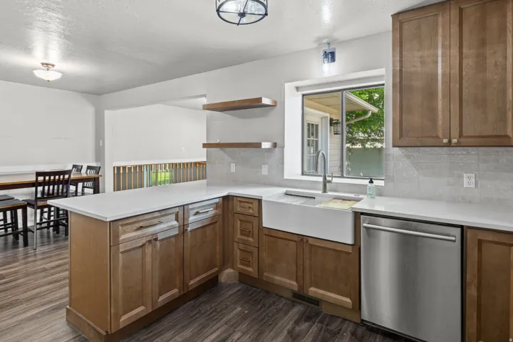 Modern kitchen featuring warm wood cabinetry, stainless steel appliances including a farmhouse sink and dishwasher, white subway tile backsplash, and a centered island with storage and counter seating