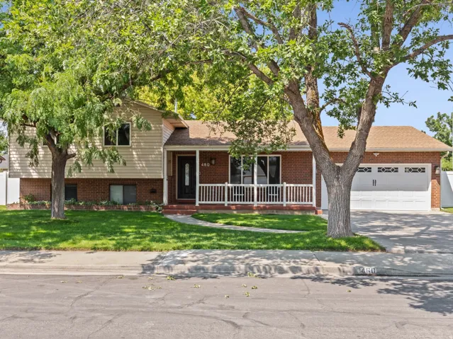 Charming two-story residence showcasing a brick and siding exterior with a welcoming front porch, mature shade trees providing natural landscaping, a manicured lawn, attached two-car garage with paneled doors, and white perimeter fencing