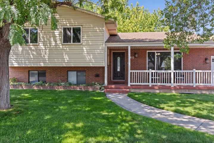Split-level brick and siding exterior with a welcoming front entry, white railing detail on the covered porch, and a manicured lawn anchored by mature shade trees