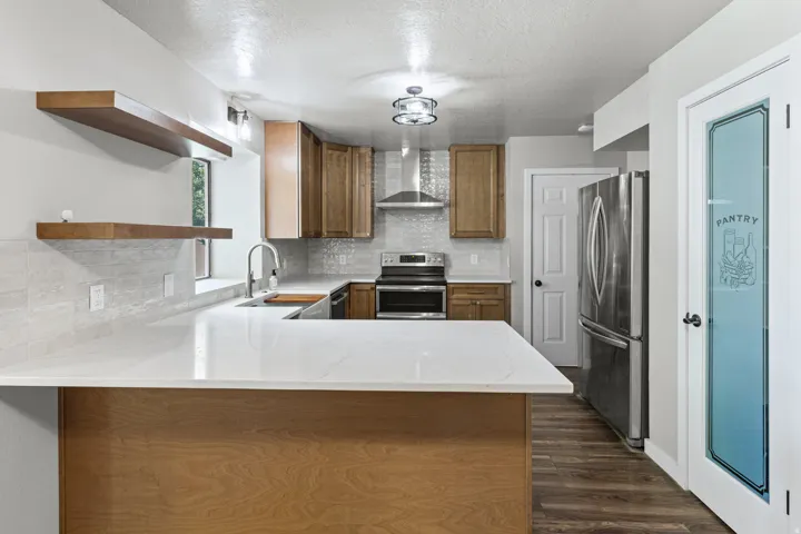 Modern kitchen featuring wood-finish flooring, white countertops, stainless steel appliances, and a glass-paneled pantry door
