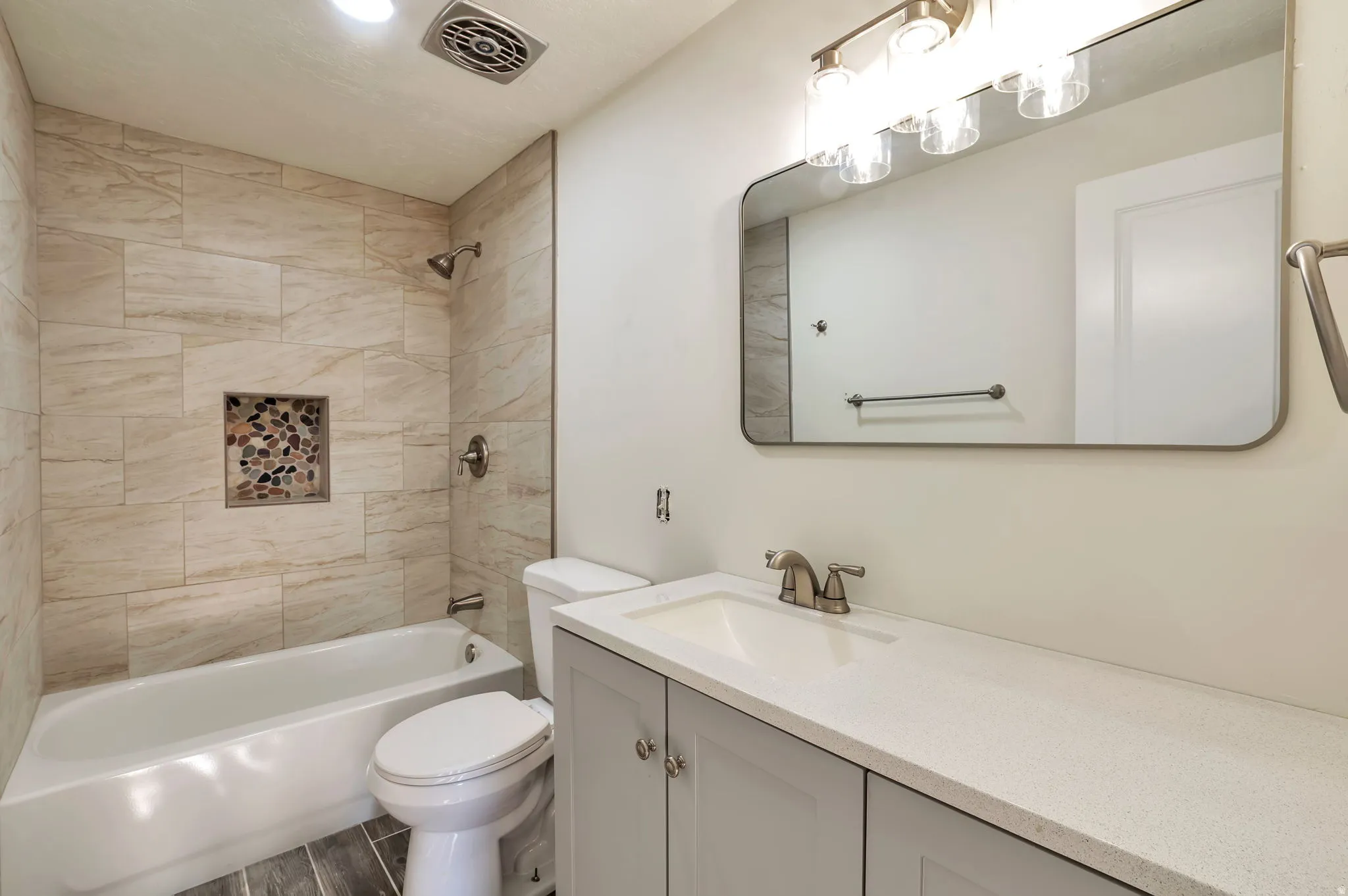 Spa-inspired bathroom featuring a frameless glass-enclosed shower with subway tile surround and integrated niche, white vanity with dual-sink configuration and quartz countertop, large framed mirror with integrated lighting, and ceramic tile flooring
