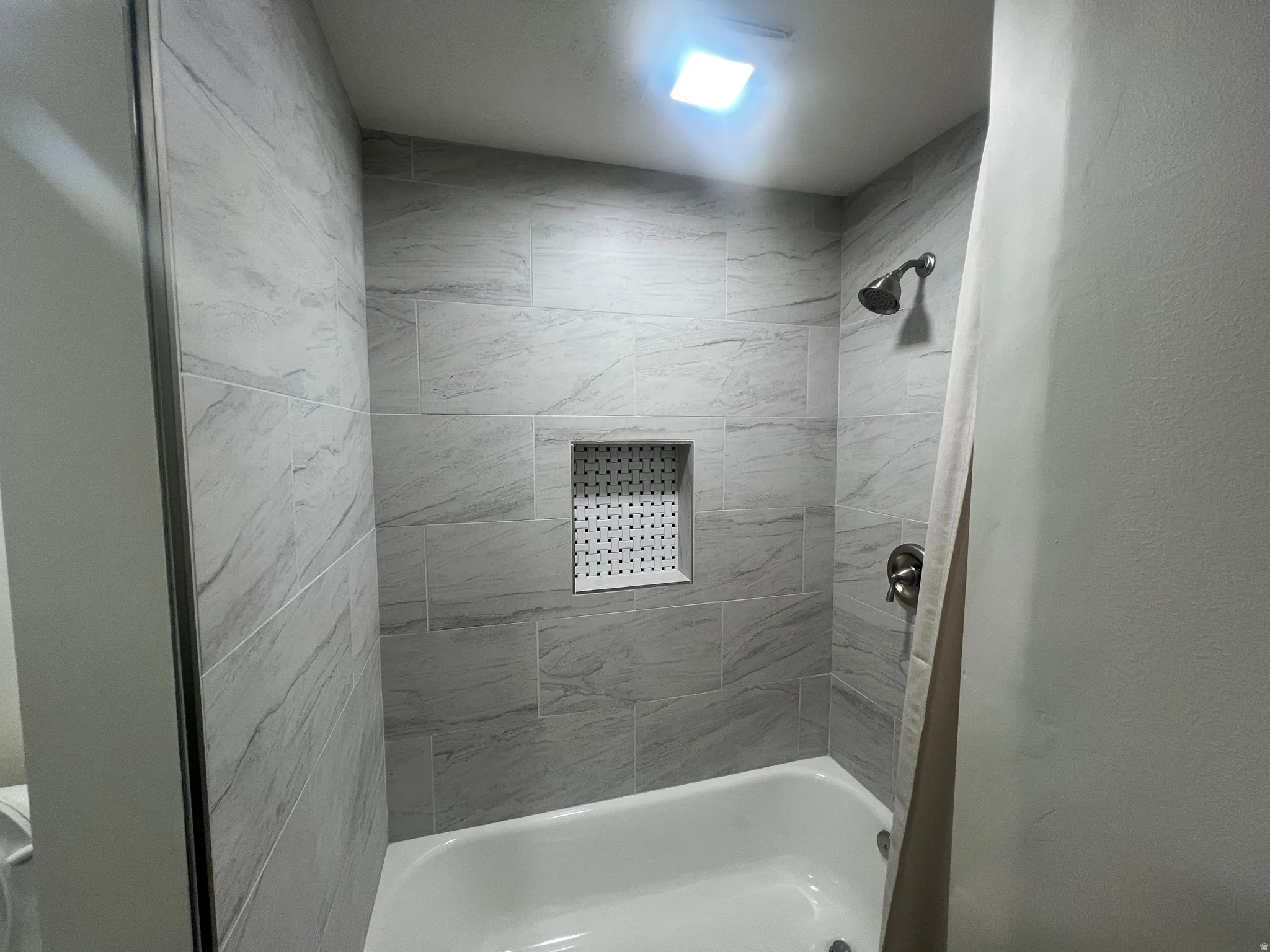 Bathtub with tiled surround, recessed shower niche, and brushed nickel fixtures