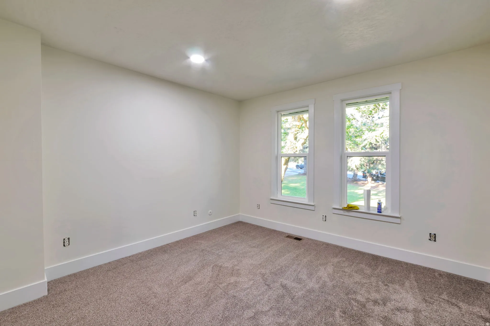 Bright corner bedroom with dual windows overlooking the exterior grounds, neutral wall finishes, and plush carpeting throughout