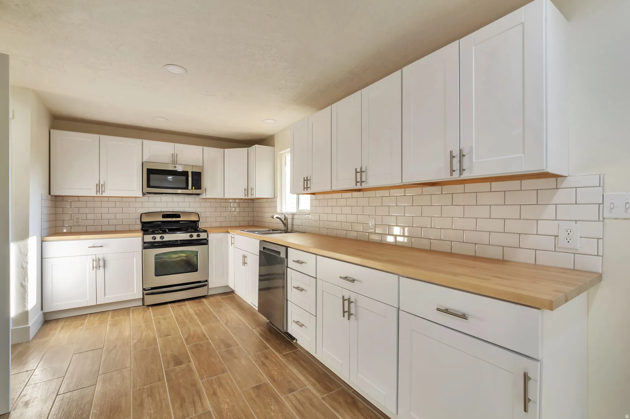 Modern kitchen featuring white shaker-style cabinetry with stainless steel hardware, wood-finish countertops, and a subway tile backsplash