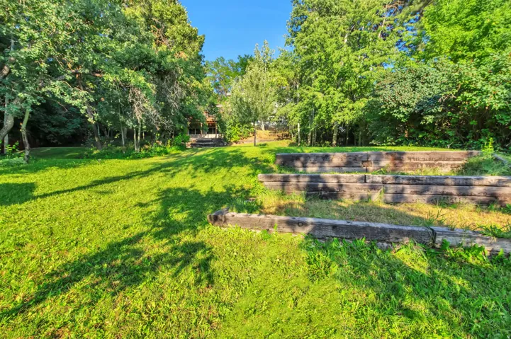 Expansive green lawn with mature trees and tiered wooden landscaping elements