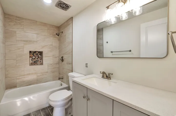 Spa-inspired bathroom featuring a frameless glass-enclosed shower with subway tile surround and integrated niche, white vanity with dual-sink configuration and quartz countertop, large framed mirror with integrated lighting, and ceramic tile flooring