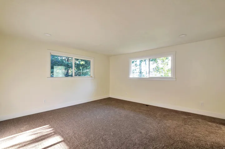 Bright, sunlit room featuring expansive windows with natural light, neutral wall finishes, and plush carpeting throughout