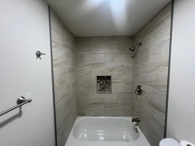 Bathtub with light-toned tiled surround, brushed nickel fixtures, and a decorative tiled shower niche