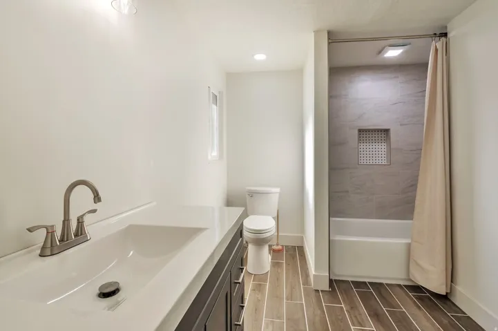 Vanity with integrated sink, brushed nickel faucet, wood-finish flooring, tiled shower surround, and built-in shower niche