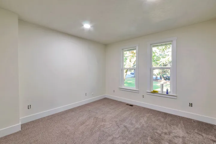 Bright corner bedroom with dual windows overlooking the exterior grounds, neutral wall finishes, and plush carpeting throughout