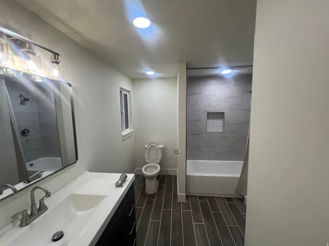 Vanity with an integrated sink and brushed nickel faucet, wood-finish flooring, recessed lighting, tiled shower surround, and built-in shower niche