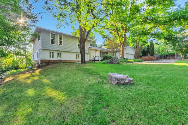 Expansive green lawn with mature trees, a multi-level residence featuring light-colored siding, and a paved driveway