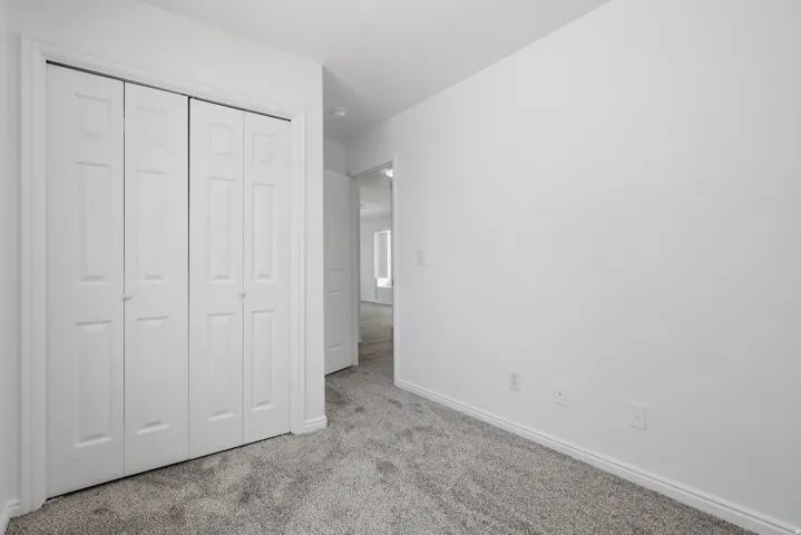 Spacious bedroom featuring neutral wall finishes, plush carpeting, and a triple-panel closet system with white six-panel doors and metal hardware