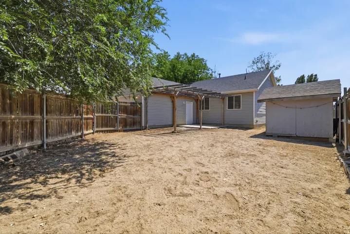 Expansive backyard featuring a concrete patio with a wooden pergola structure, a detached storage shed, and a privacy fence