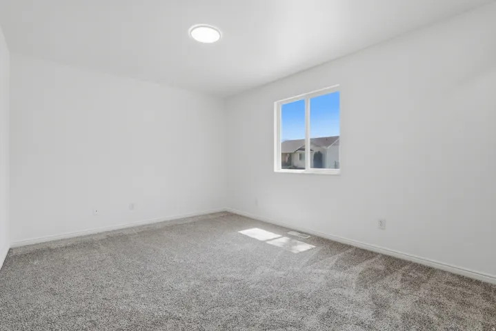 Bright interior space featuring a window with natural light, neutral wall paint, gray carpet flooring, and a recessed ceiling light fixture