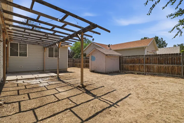 Spacious backyard retreat featuring a wooden pergola structure with lattice detailing, level sandy ground, wooden privacy fencing, and a detached storage shed