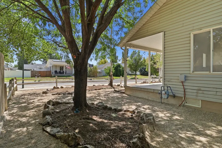 Exterior featuring a covered porch with a concrete foundation, horizontal siding, and a prominent mature tree with a rock border