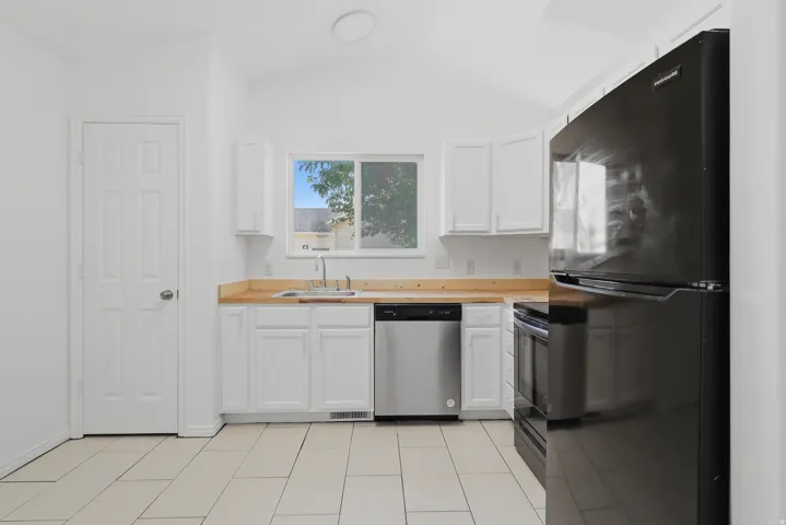Kitchen featuring white cabinetry, light wood-finish countertops, stainless steel dishwasher, and black refrigerator