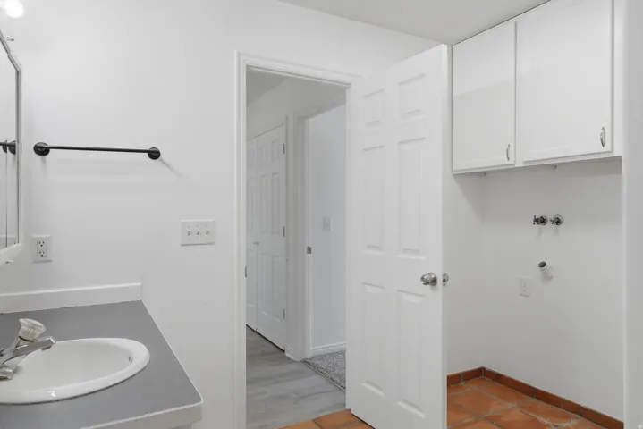 Utility area with white cabinetry, terra cotta flooring, and plumbing connections for appliances
