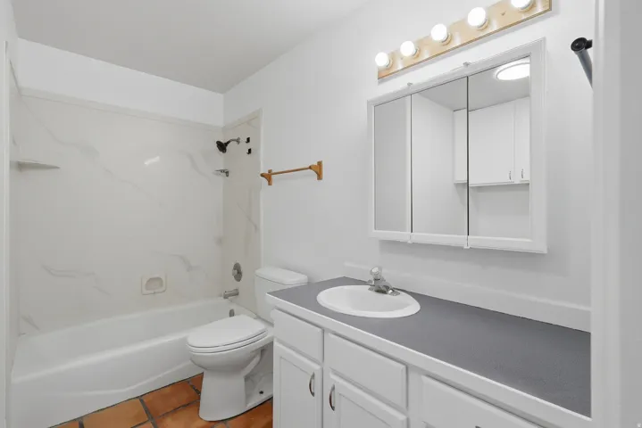 Bathroom featuring a white vanity with integrated sink, a medicine cabinet, a full-size bathtub with shower, and terra cotta-style floor tiles