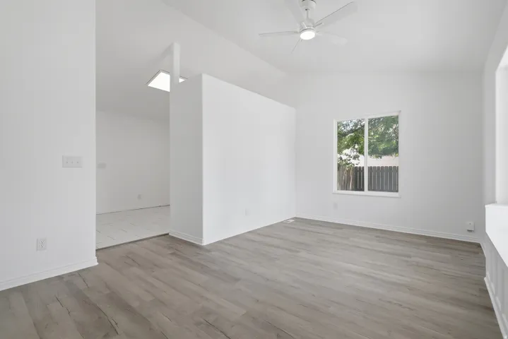 Spacious room with wood-finish flooring, white walls, and a ceiling fan