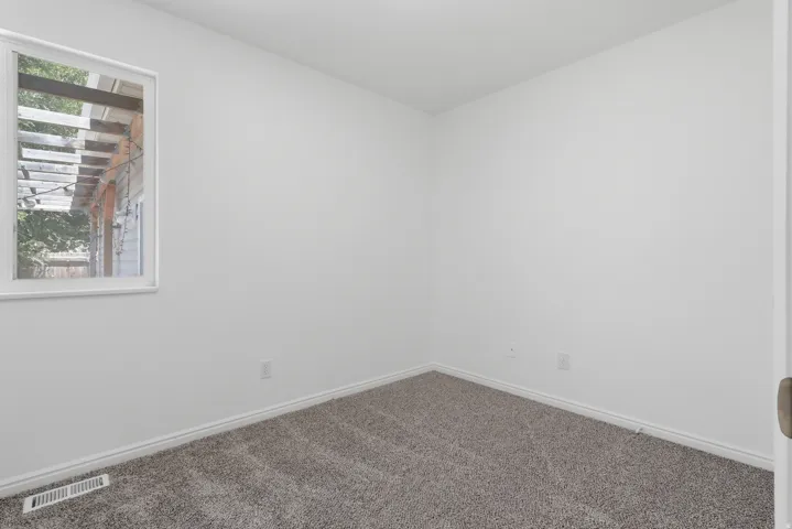Room featuring neutral wall paint, gray carpeting, white trim, and a window providing natural light