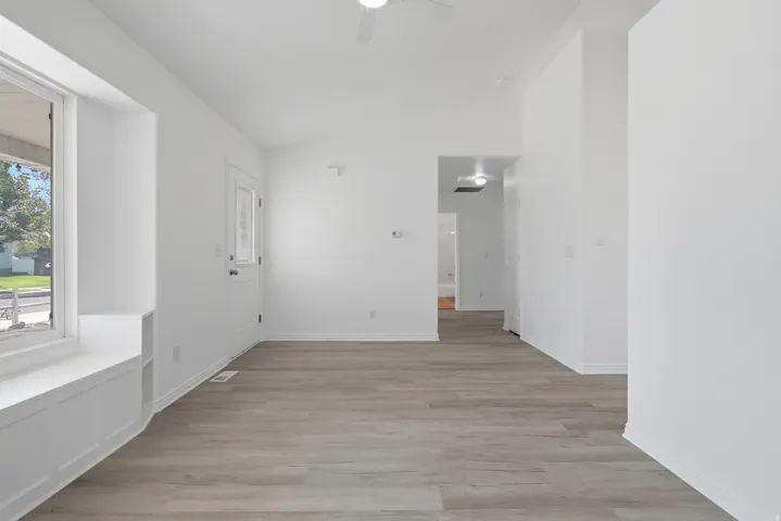 Spacious room featuring wood-finish flooring, white walls, and a prominent window with a built-in window seat