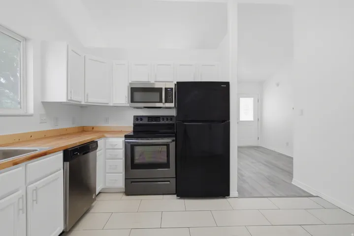 Kitchen featuring white cabinetry, light wood-finish countertops, and stainless steel appliances including a microwave, range, and dishwasher