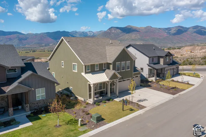 Two-story residence featuring vertical siding, a covered front porch with timber-frame accents, a concrete driveway, an attached multi-car garage, and a mountainous backdrop
