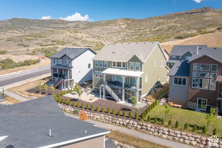 Two-story residence featuring vertical siding, a covered upper-level deck, a stone-retaining wall, a paved patio area, and a mountain backdrop