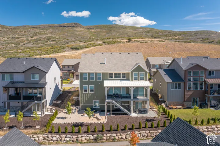 Multi-level residence featuring vertical siding, a covered upper-level deck with metal roofing, a walk-out basement, and a landscaped rear yard with stone retaining walls, set against a mountainous backdrop