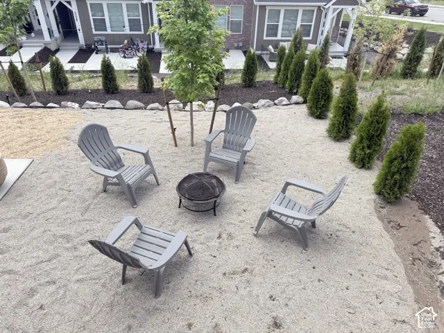 Gravel outdoor seating area featuring a central fire pit, bordered by a row of evergreen shrubs and a young deciduous tree