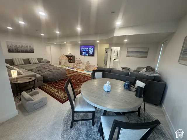 Spacious recreation room featuring recessed lighting, light-toned carpeting, and a round wood-finish dining table with upholstered chairs