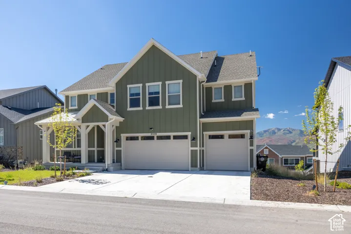 Two-story exterior featuring vertical siding, a covered front porch with gable roof detailing, three-car garage, and a mountain backdrop