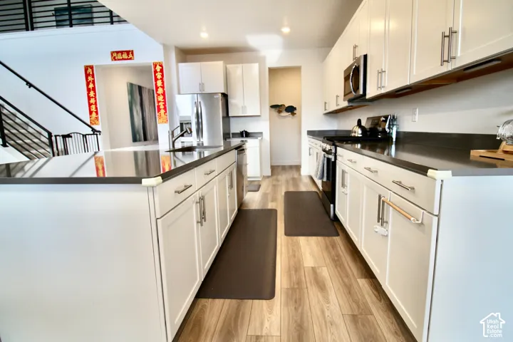 Modern kitchen featuring white shaker-style cabinetry, dark countertops, and wood-finish flooring