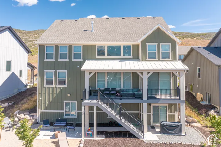 Two-story residence featuring vertical siding, a covered upper deck with metal roof, a lower-level concrete patio, and stairs with metal railings