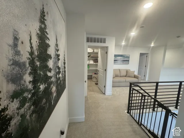 Upper-level landing featuring a contemporary metal railing, recessed lighting, and soft carpet flooring