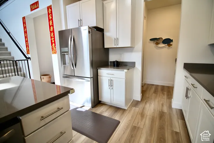 Modern kitchen featuring white cabinetry, stainless steel refrigerator, dark countertops, wood-finish flooring, and brushed nickel hardware