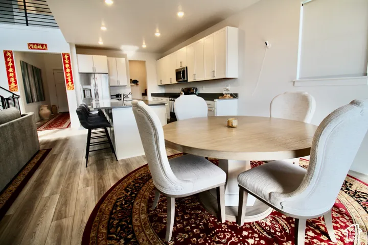 Open-concept living space with wood-finish flooring, recessed lighting, and a kitchen featuring stainless steel appliances, white cabinetry, and dark countertops