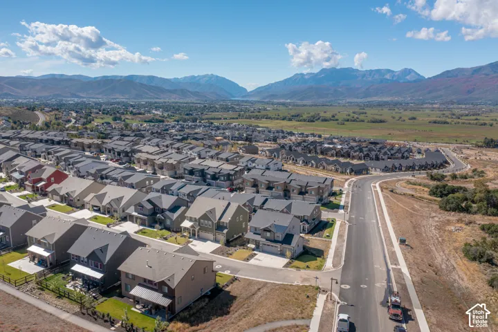 Aerial perspective of a suburban neighborhood featuring multi-level residential structures, asphalt roadways, concrete sidewalks, and a prominent mountain range backdrop