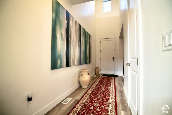 Entryway featuring light-toned wood-finish flooring, a white paneled door, high ceilings, and a transom window providing natural light
