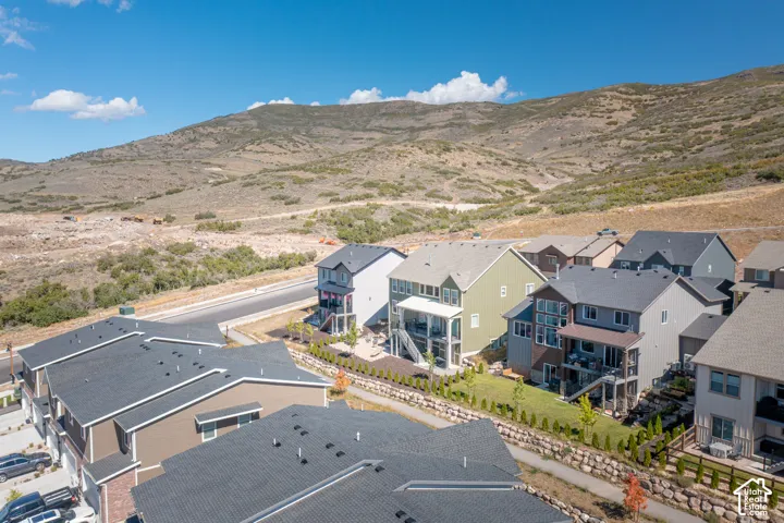 Aerial perspective of residential structures featuring multi-story architectural designs, pitched shingle roofing, integrated rear decks, and proximity to mountainous terrain