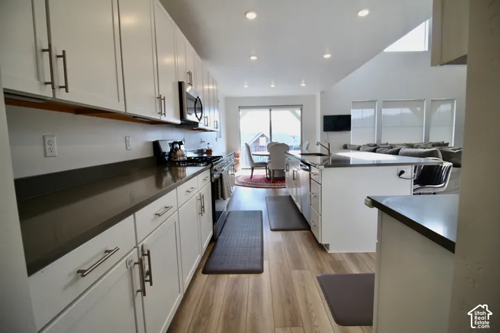 Open concept kitchen featuring light wood-finish flooring, white cabinetry with contemporary hardware, dark countertops, a kitchen island with seating, and recessed lighting