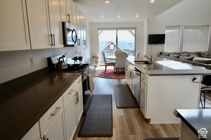 Modern kitchen featuring a gas range, built-in microwave, white shaker cabinetry with dark hardware, and light wood-finish flooring