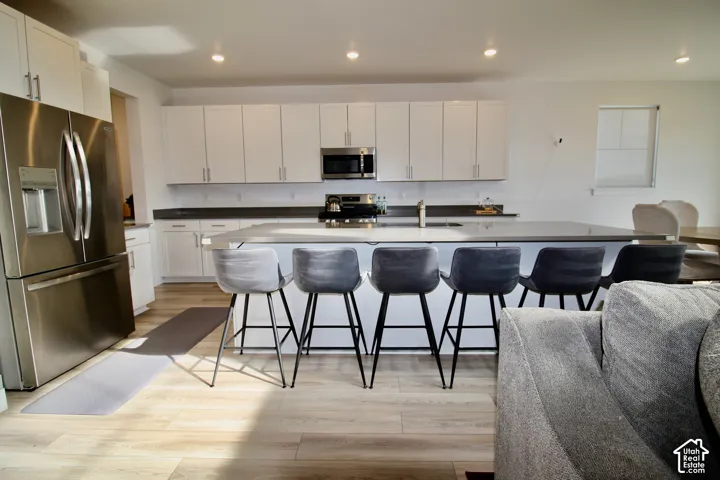 Kitchen featuring a large island with counter seating, stainless steel appliances, light-toned wood-finish flooring, white cabinetry, and recessed lighting