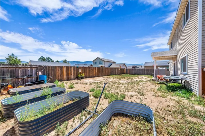 Expansive backyard space with a wood privacy fence, covered patio, and raised garden beds