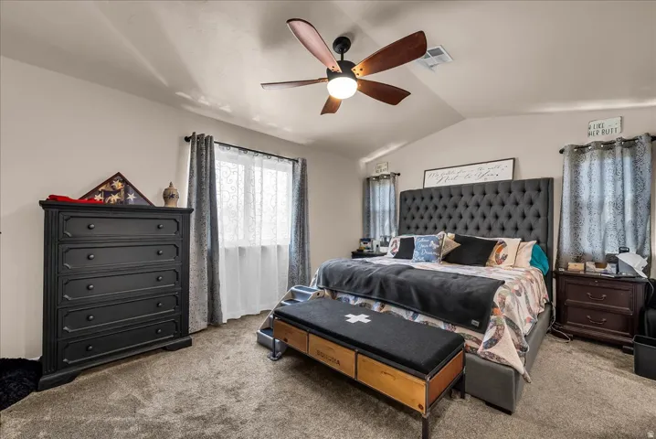 Vaulted ceiling, ceiling fan with integrated lighting, two windows with curtain rods, wall-to-wall carpeting